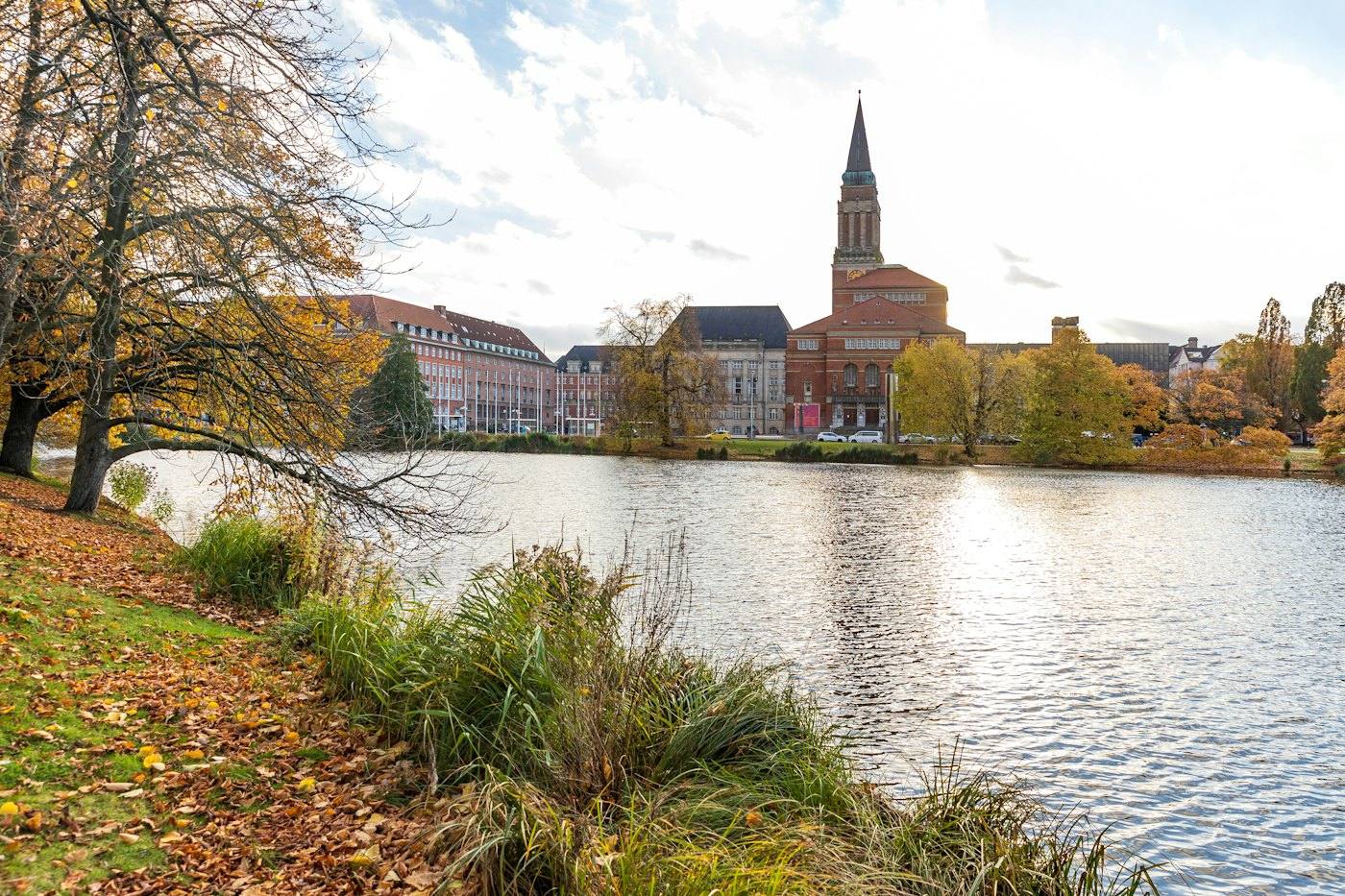 Lake in autumn with the town-hall tower and buildings behind