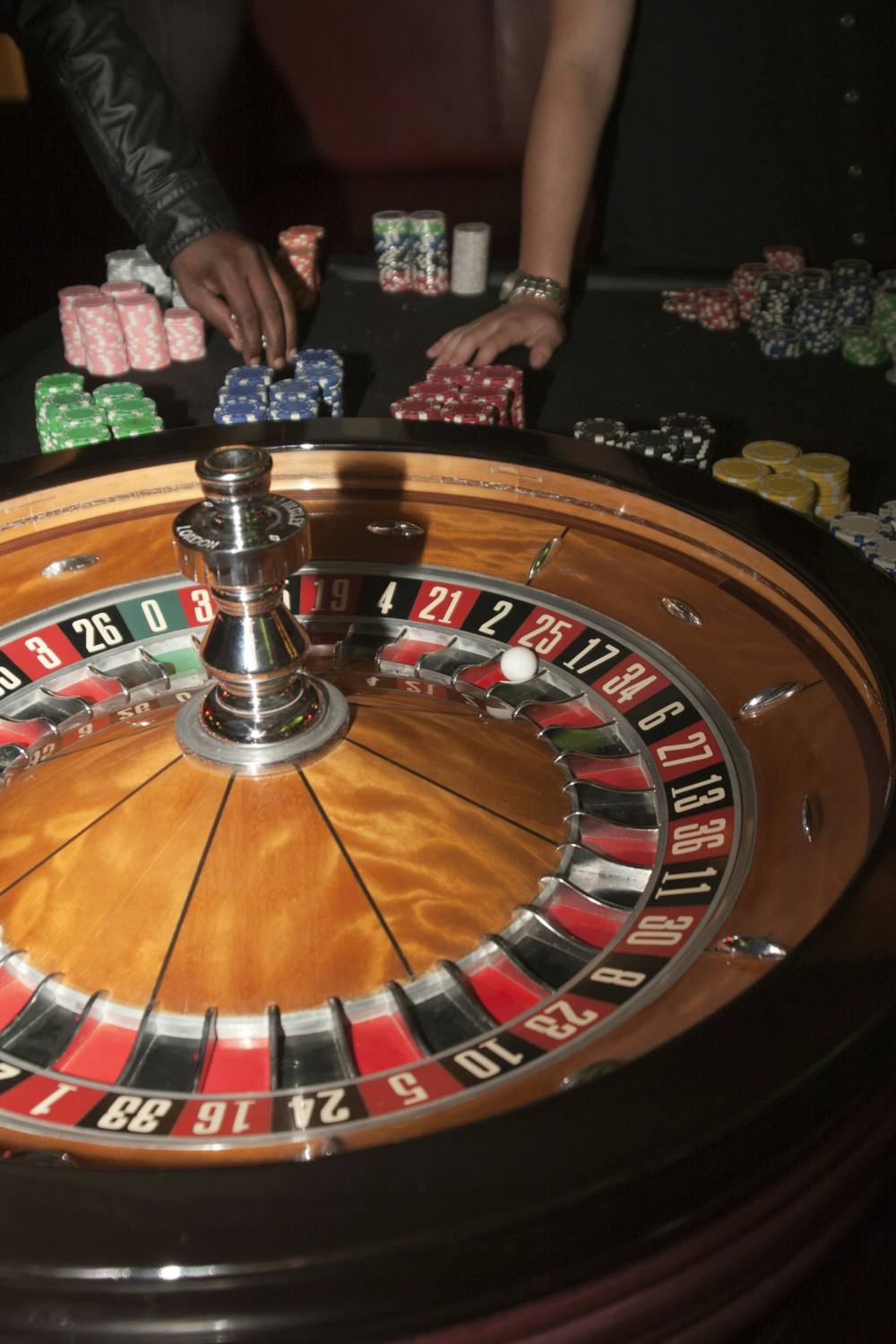 Roulette wheel from above, hands with chips behind
